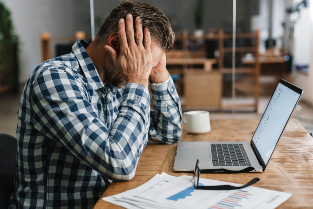 Unhappy grey man with headache working with laptop in office