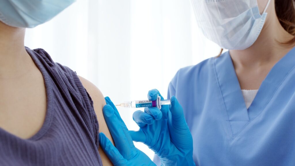 Practitioner vaccinating woman patient in clinic. Doctor giving injection to adult woman