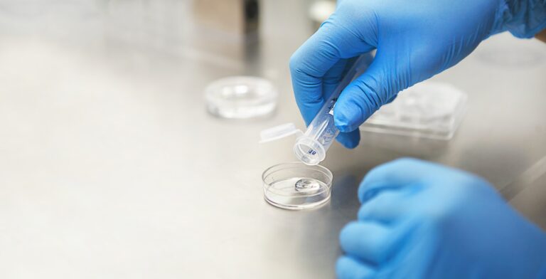 Hands of a scientist in the laboratory with a test tube and a microscope.