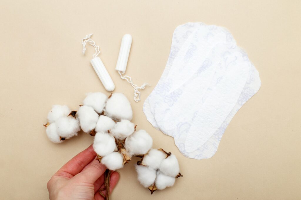 Women's hand holds flower cotton near hygiene pads with tampons on a beige background