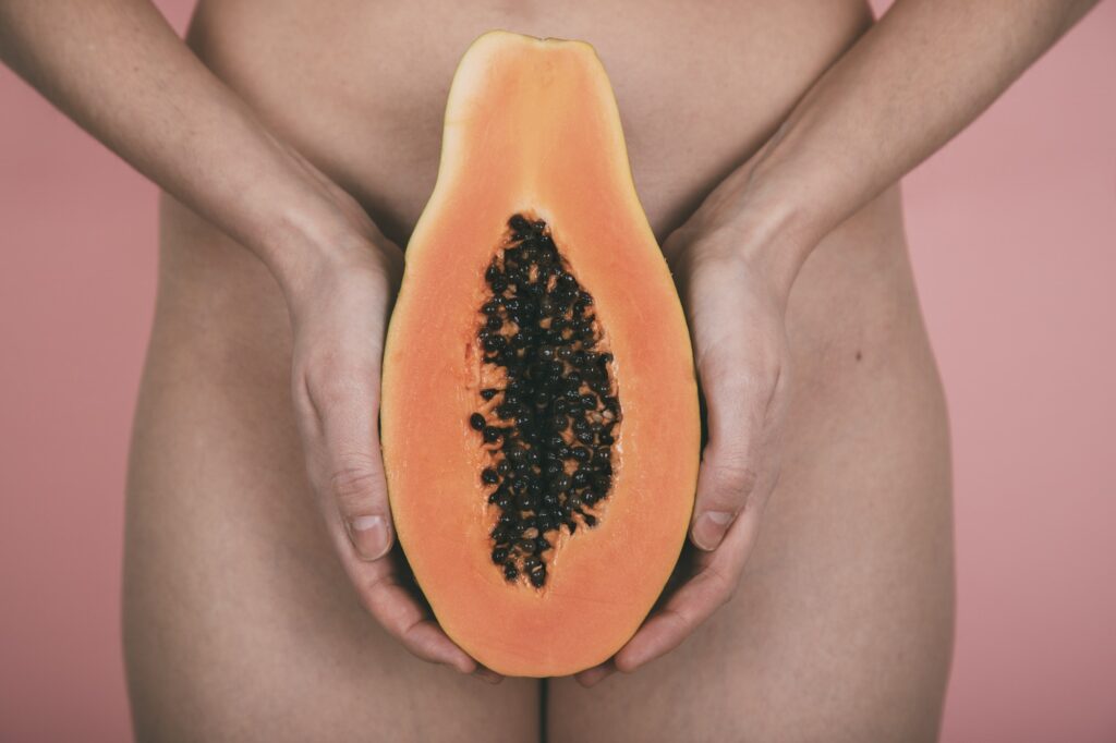 Woman hands hold a papaya in front of the hips. Pink background.