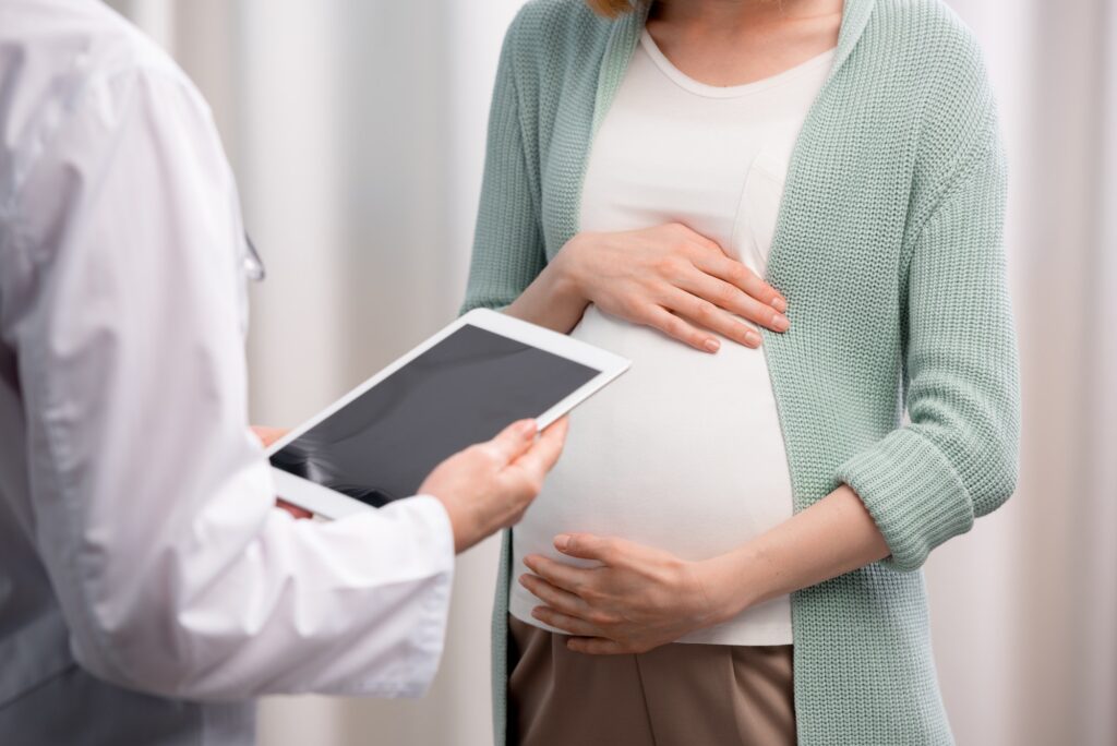 partial view of doctor and pregnant woman discussing pregnancy process together in clinic
