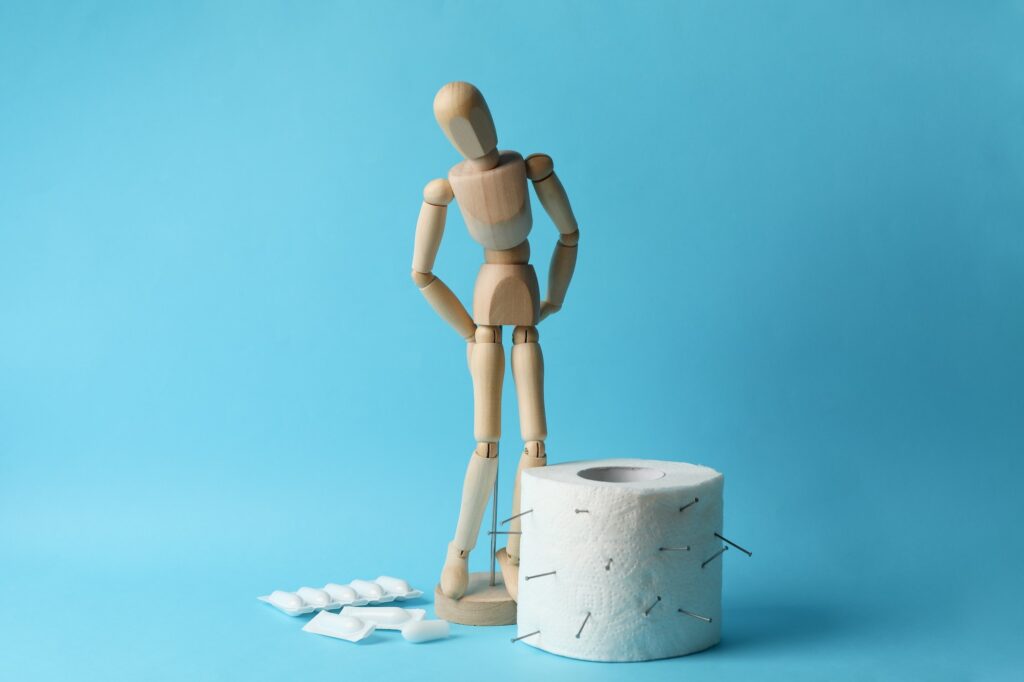 Wooden man, candles and toilet paper on blue background. Hemorrhoids