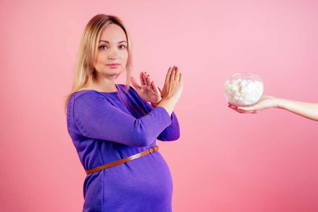 Beautiful blonde pregnant woman in a violet dress with big baby bump refuses sugar