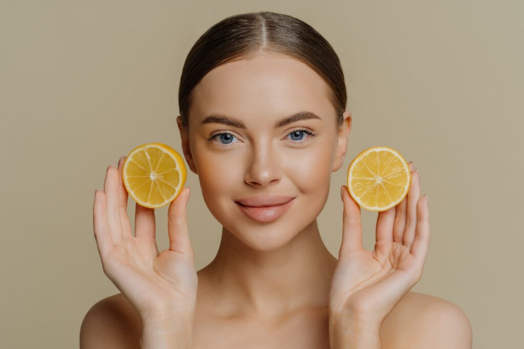 Beautiful brunette woman holds juicy lemon slices has healthy shiny skin gets vitamins from citrus