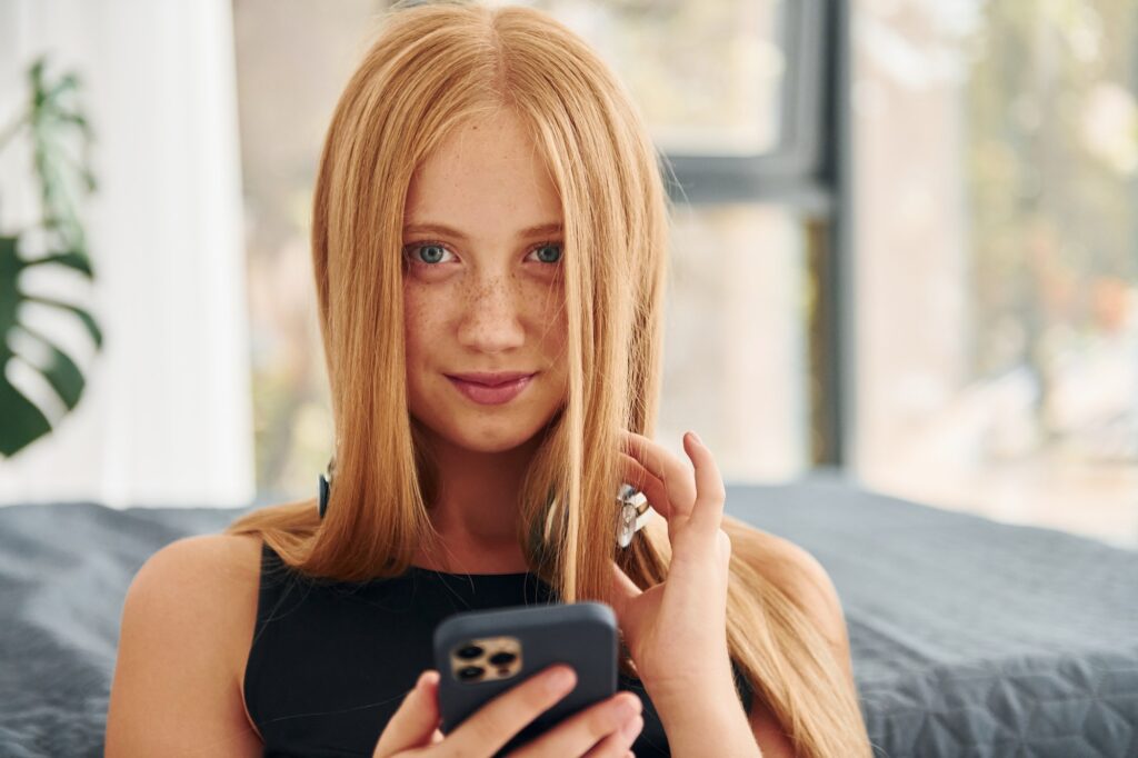 In headphones. Female teenager with blonde hair is at home at daytime