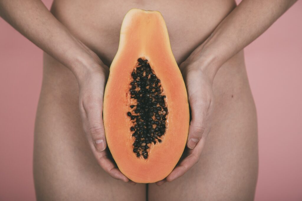 Woman hands hold a papaya in front of the hips. Pink background.