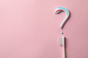 Question mark made of toothpaste and toothbrush on pink background