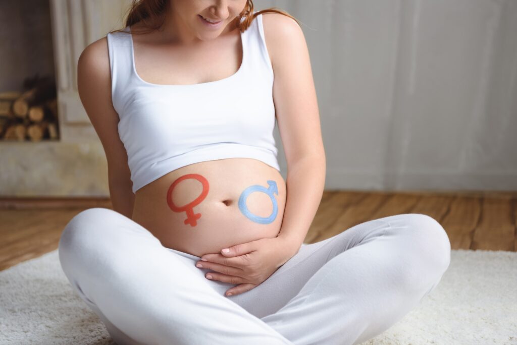 cropped view of pregnant woman with boy or girl symbols on her belly sitting on floor at home