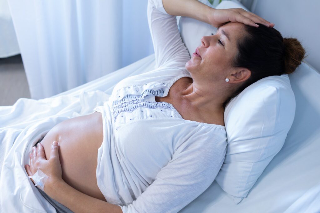 High angle view of Caucasian pregnant woman suffering from pain while touching her belly in the ward