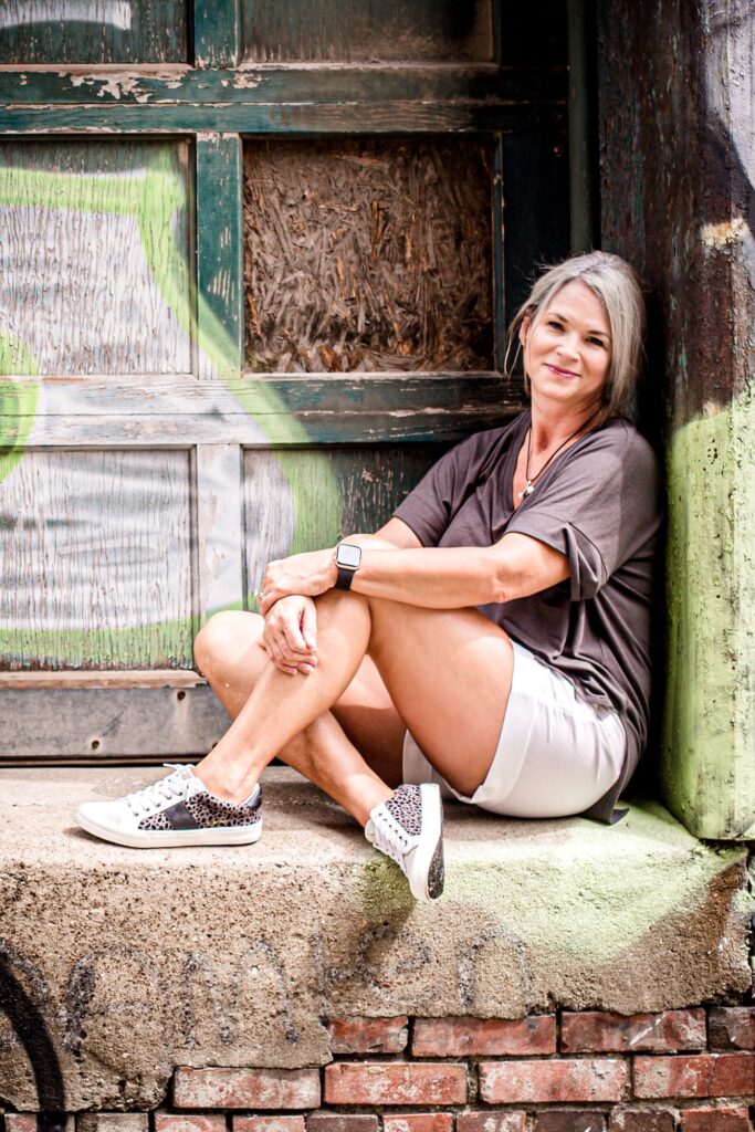 Middle aged woman sitting on brick with graffiti background.