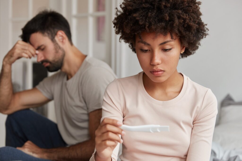 Upset dark skinned attractive woman looks at pregnancy test, suffers from infertility, frustrated hu