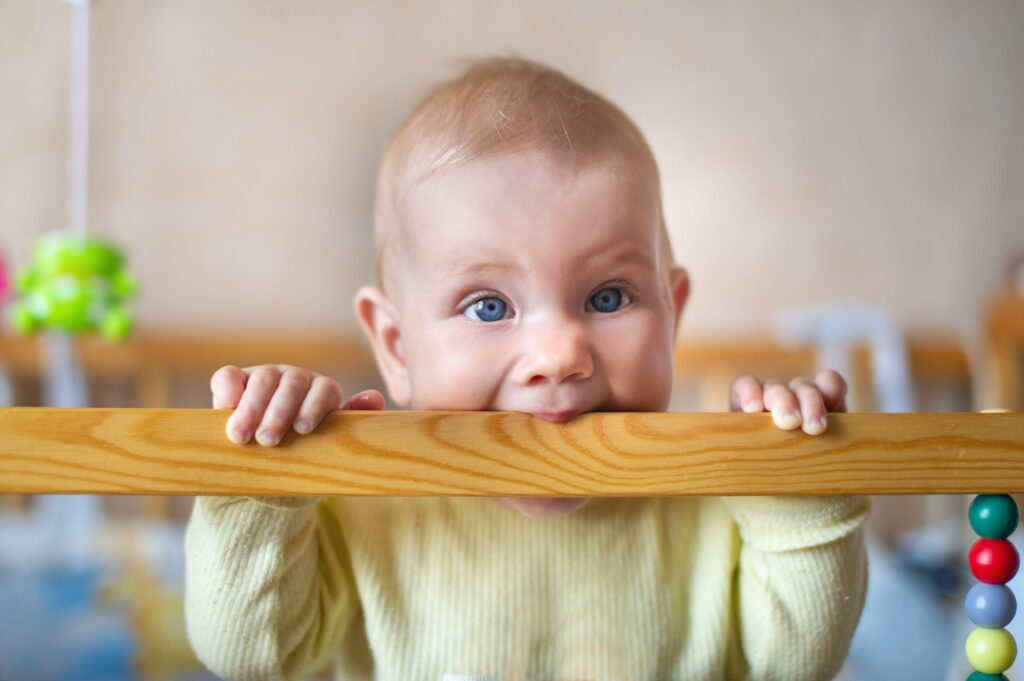 Closeup portrait of lonely toddler bites wooden bed frame. Child concept