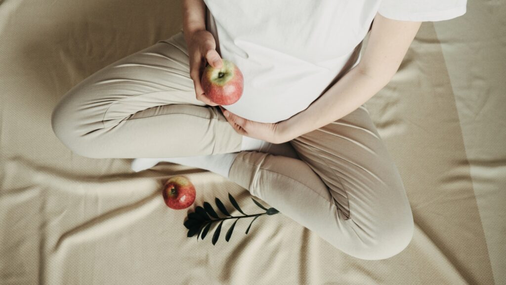 Healthy food, vegan low sugar diet concept. Pregnant woman eating apple at home.