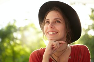 Horizontal portrait of pretty elegant female in summer hat and red shirt having good mood and smilin