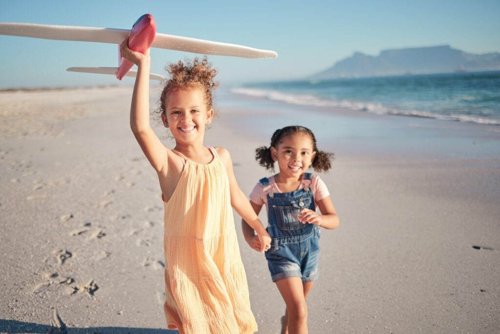 Toy airplane, beach and children running with a happy, sun and joy mindset in the nature sun. Kids,