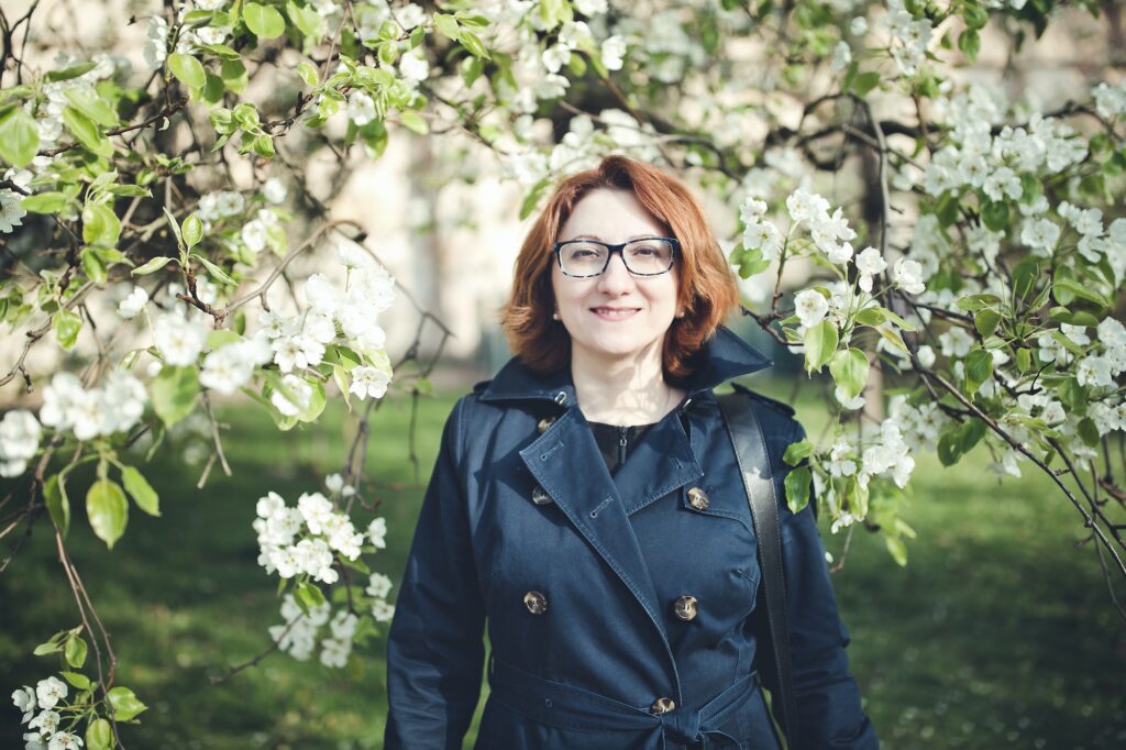 Confedent middle aged Armenian woman in a blue trench coat under the blooming tree.
