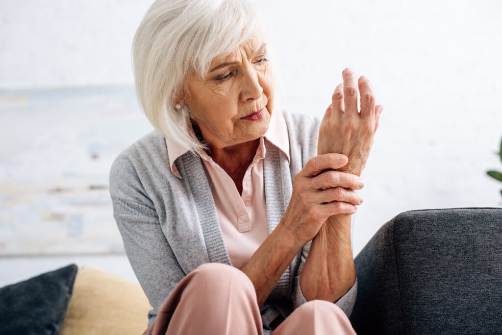 senior woman having hand Arthritis and sitting on sofa in apartment
