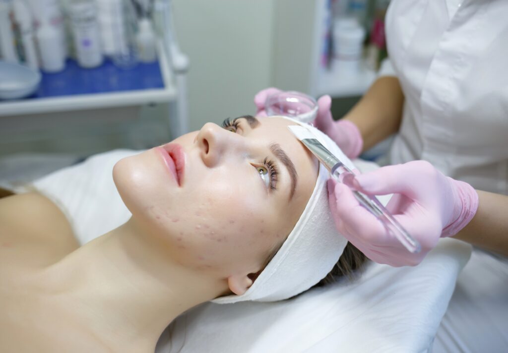 cosmeiologist applies a mask to a young woman with acne