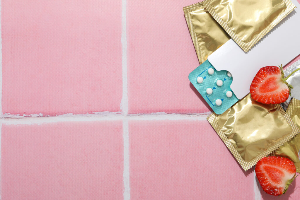 Condoms, strawberries and birth control pills on a pink background, place for text