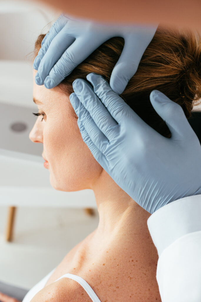 cropped view of dermatologist in latex gloves examining hair of patient in clinic