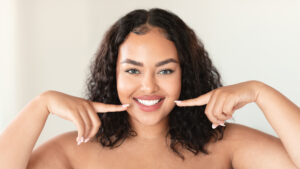 Oral care concept. Beautiful plus size woman pointing at her perfect smile with two fingers, showing