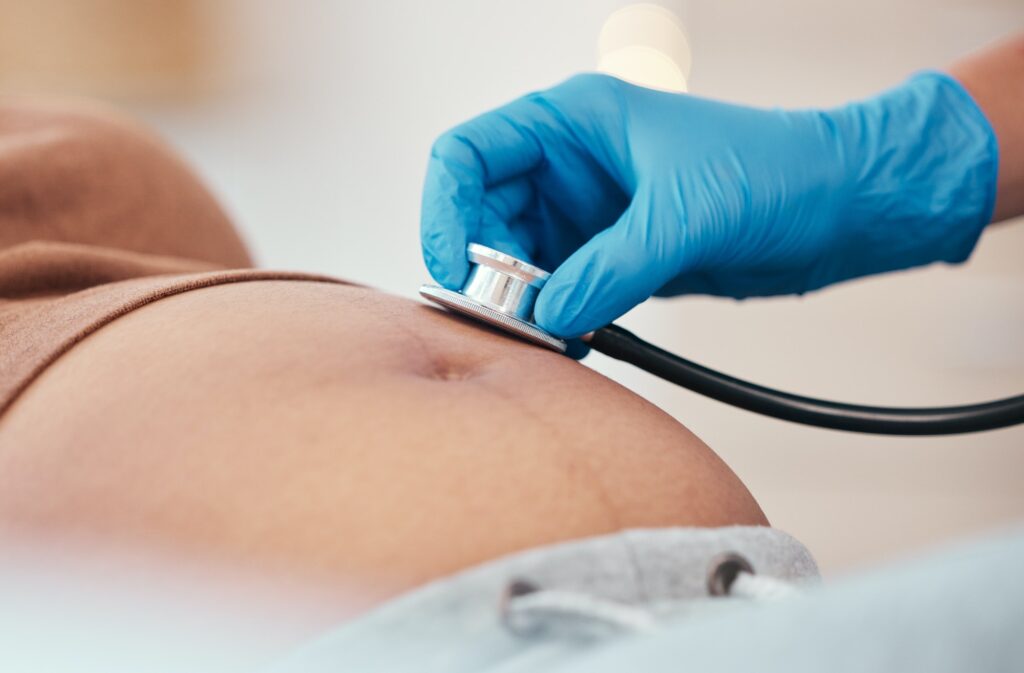 Hand, stethoscope and the belly of a woman pregnant in a hospital for prenatal exam or checkup in t