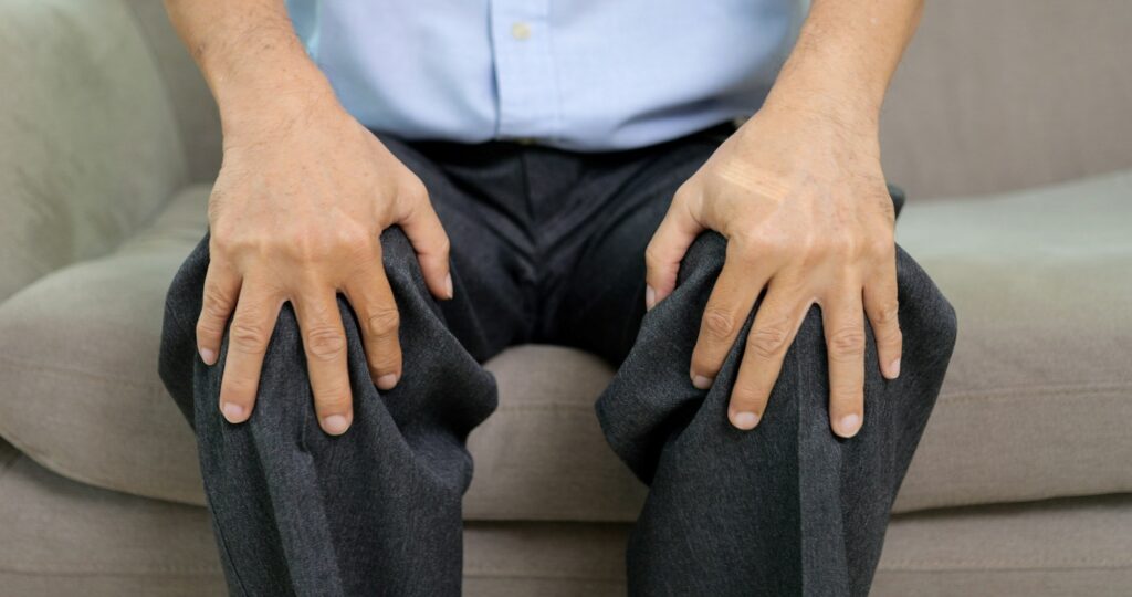 Close up view of senior grandfather suffering from knee pain sitting on sofa