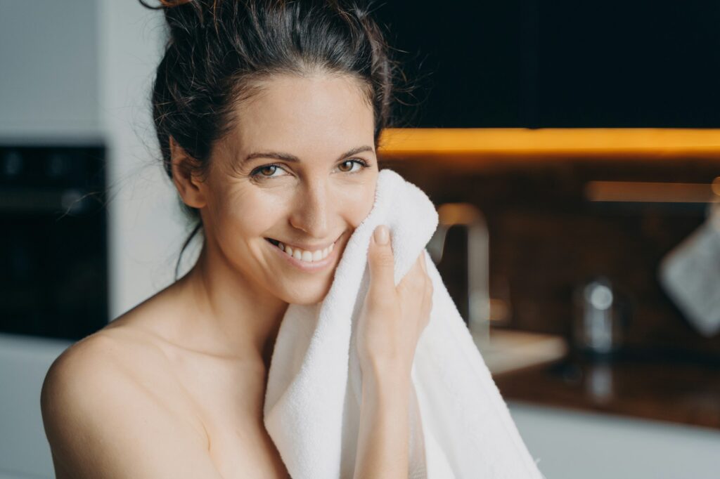 Caucasian woman is wiping face with towel and smiling. Hygiene, dermatology and skin cleansing.