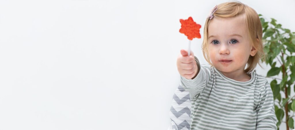 Cute little kid, baby girl sitting at chair on white background at home eating sugar candy
