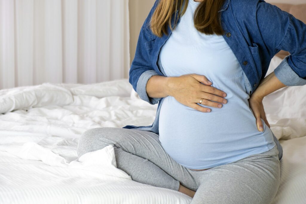 Pregnant woman touch her tummy and keep one hand on her back.