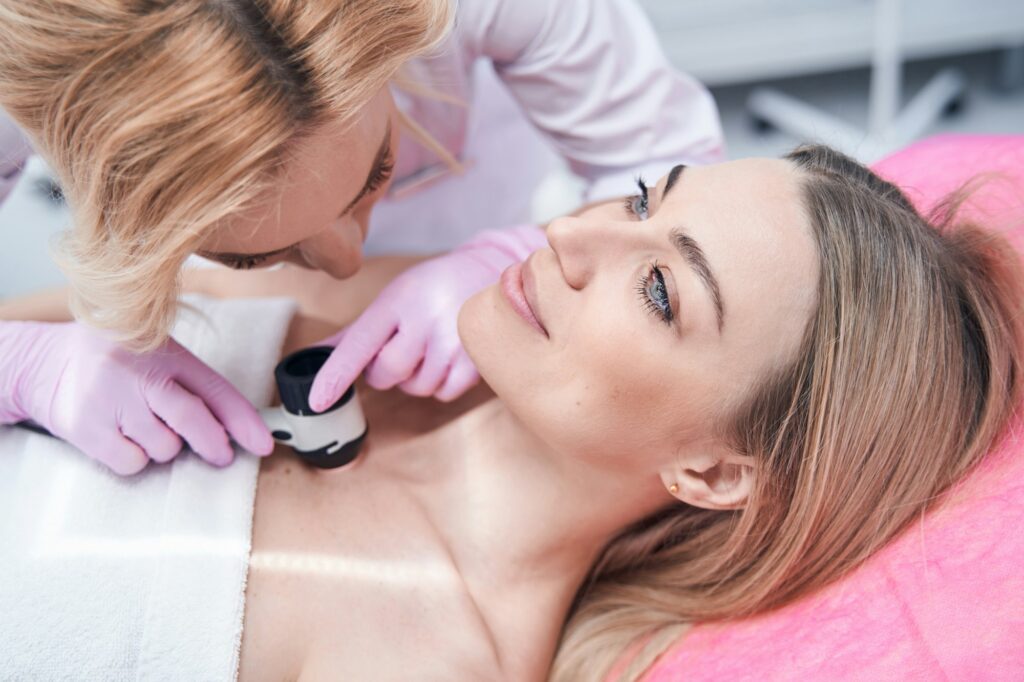 Experienced dermatologist checking moles on skin of young woman