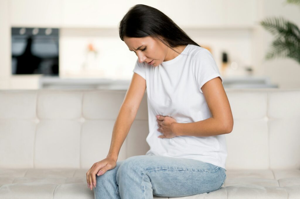 Frustrated young caucasian woman, sitting on the sofa in the living room, experiencing abdominal