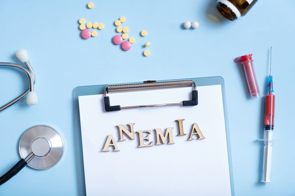 Anemia text with stethoscope, pills and syringe flat lay, top view