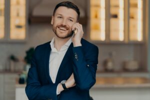 Smiling stylish man standing relaxed in living room and talking on mobile phone