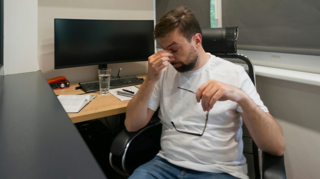 Tired overworked man taking off glasses rubbing tired dry eyes after long pc computer work
