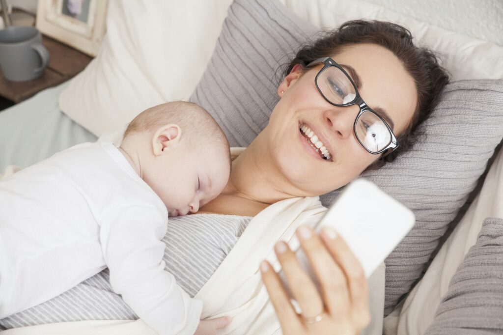 Baby boy sleeping on mother, mother using smartphone
