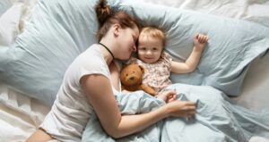 Mom Caucasian woman in pajamas with baby sleeping on bed, top view. Early morning mom and baby