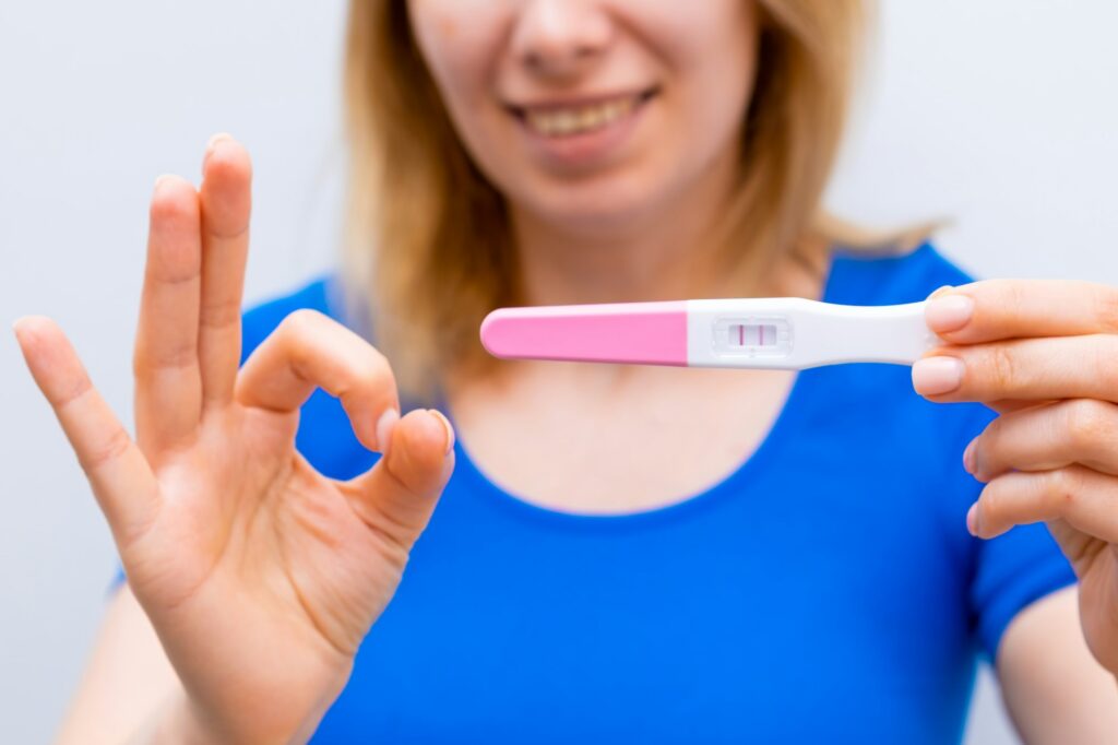 Smiling woman shows sign ok and holding a positive pregnancy test