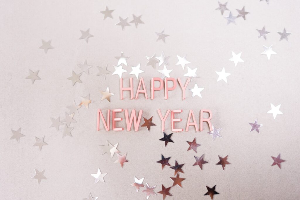 Happy new year's greetings on pink background with silver stars confetti