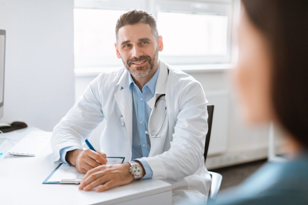Medical check up. Male doctor talking with female patient, writing personal information, filling